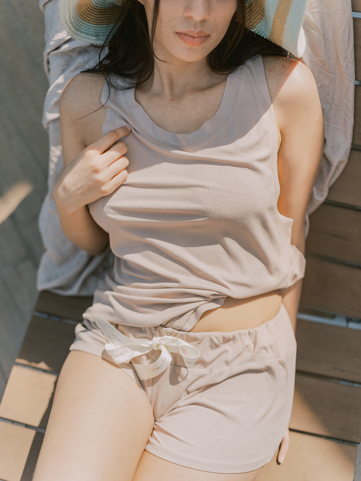 Woman wearing a beige tank top and shorts sitting on a wooden bench.